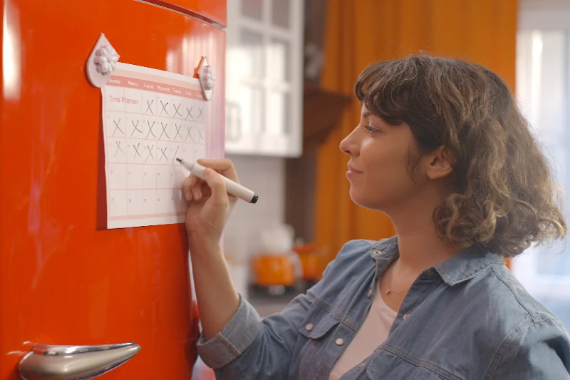 Woman marking off her calendar hanging on a fridge